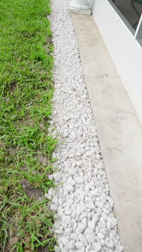 White stone strip beside grass and a screened exterior wall